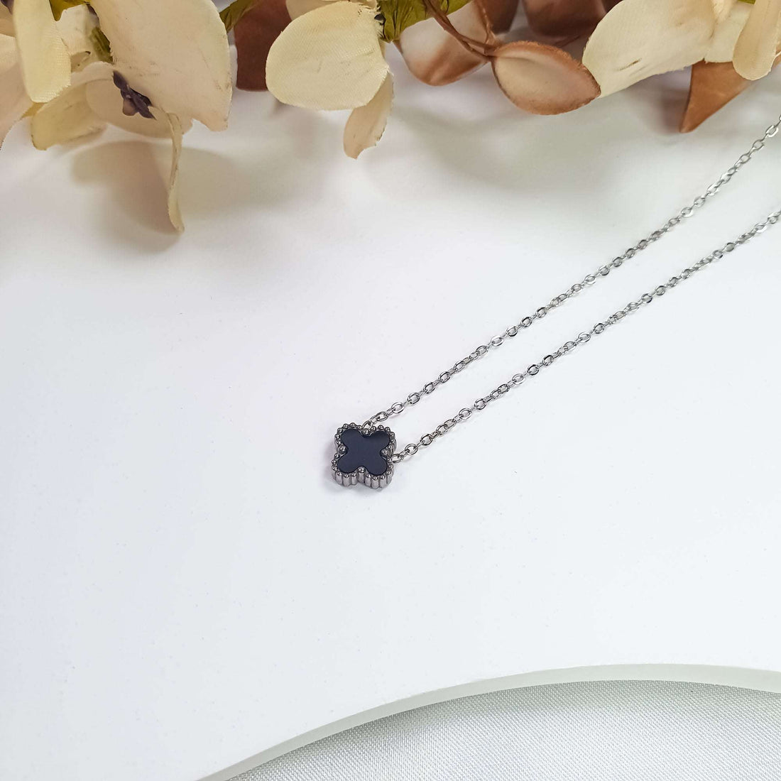 Black clover necklace in close-up on a light surface with flowers