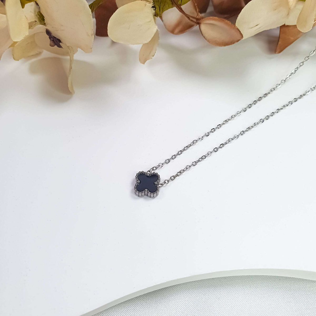 Black clover necklace in close-up on a light surface with flowers