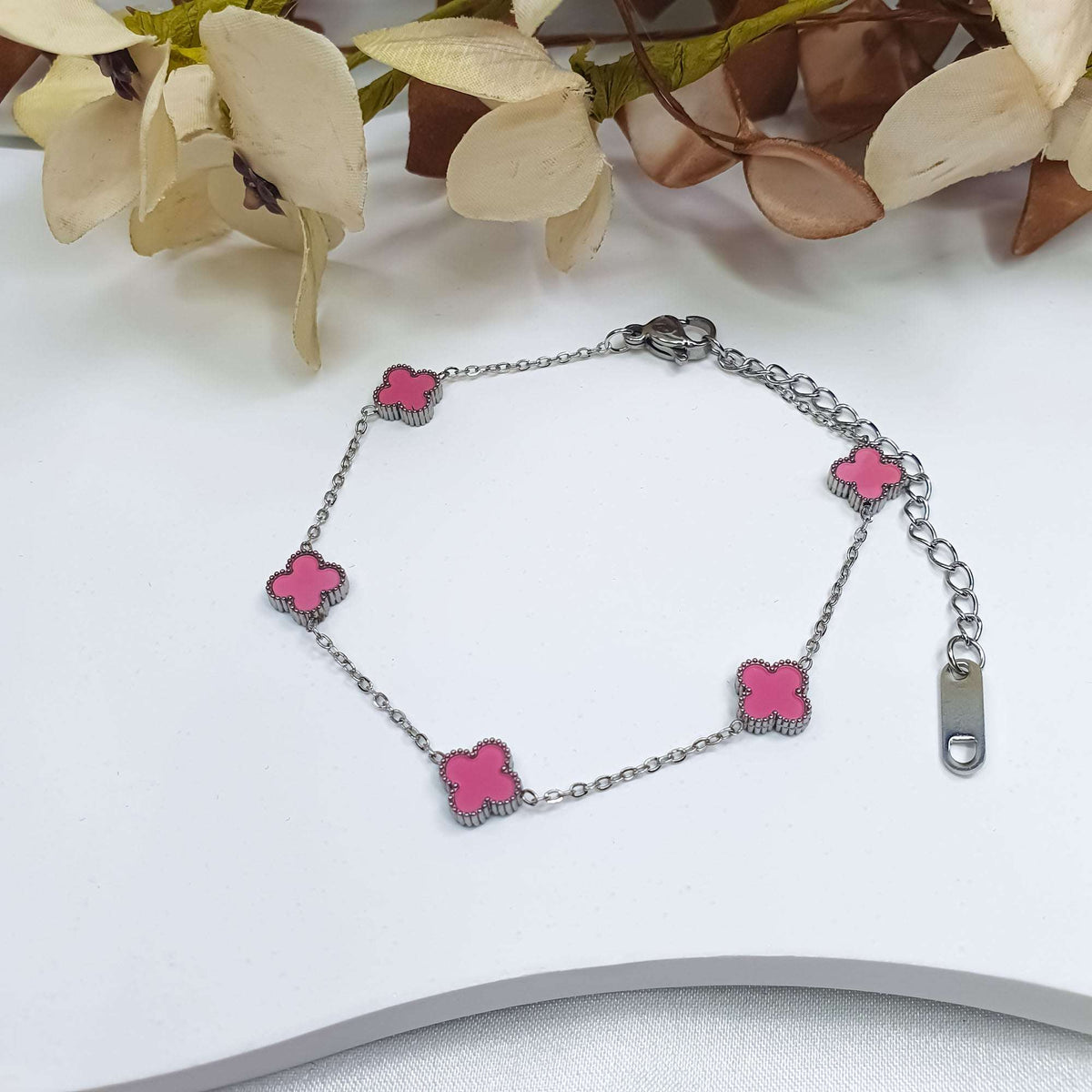 Pink clover chain bracelet on a light surface beside dried flowers