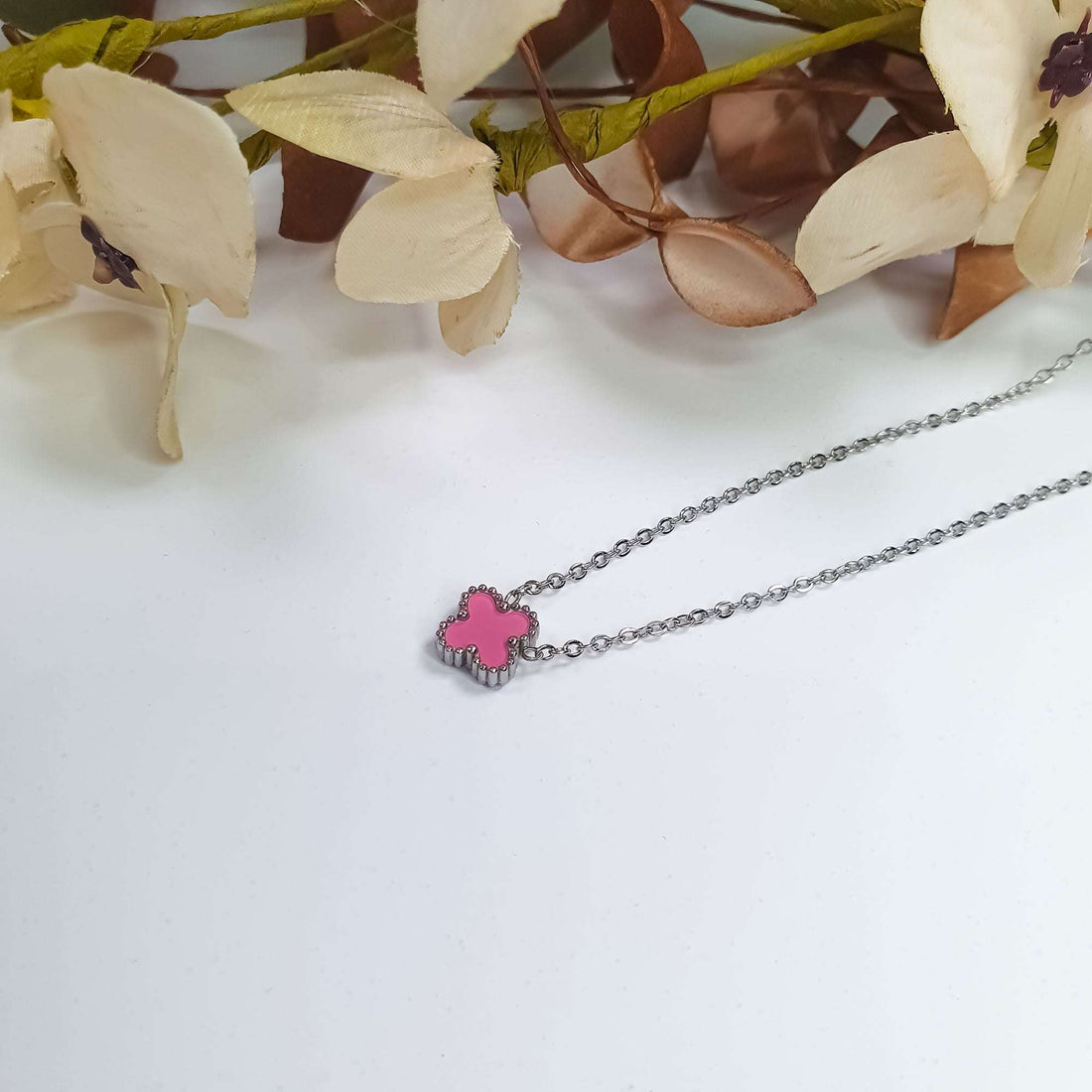 Silver-tone chain with a pink enamel clover pendant on a light surface