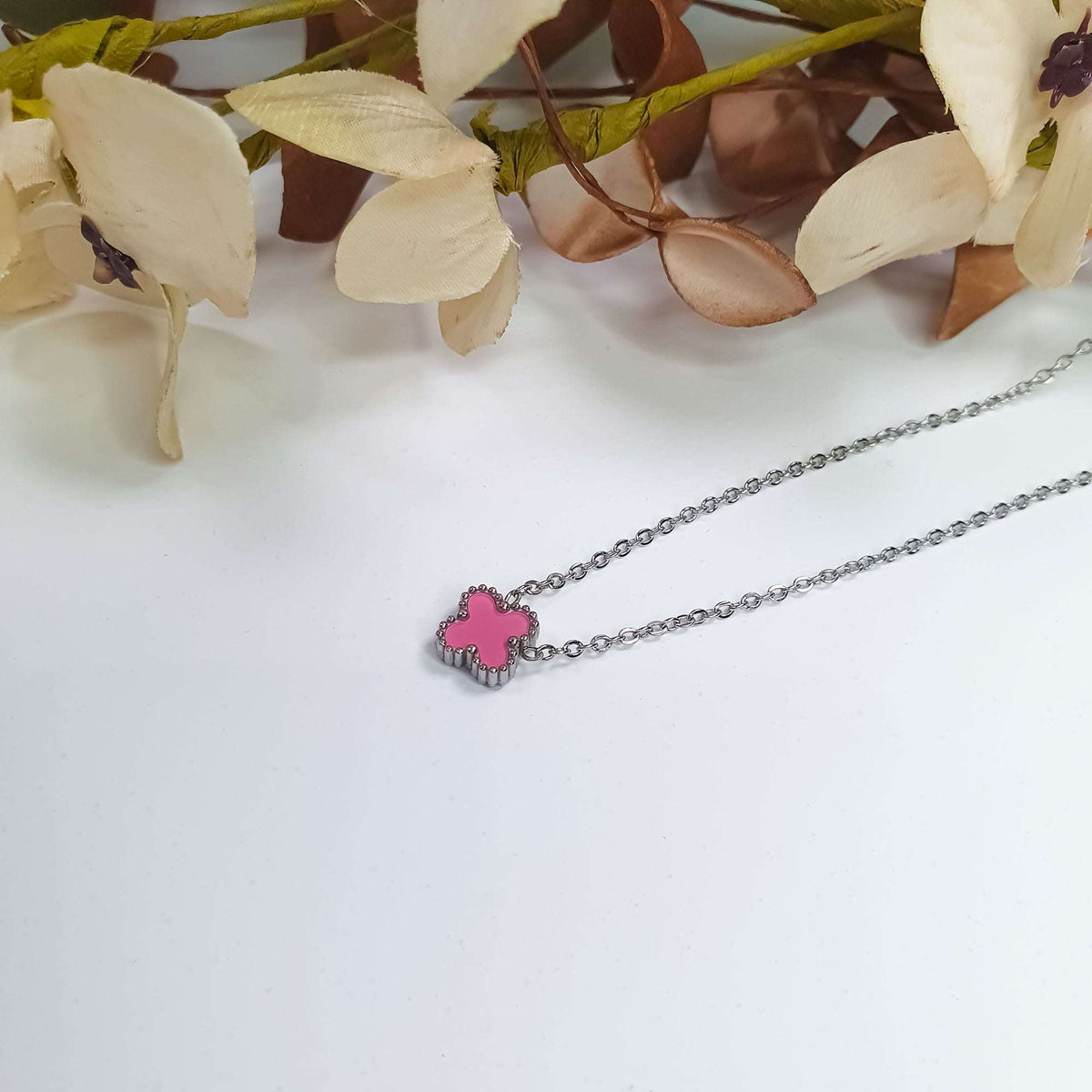 Silver-tone chain with a pink enamel clover pendant on a light surface