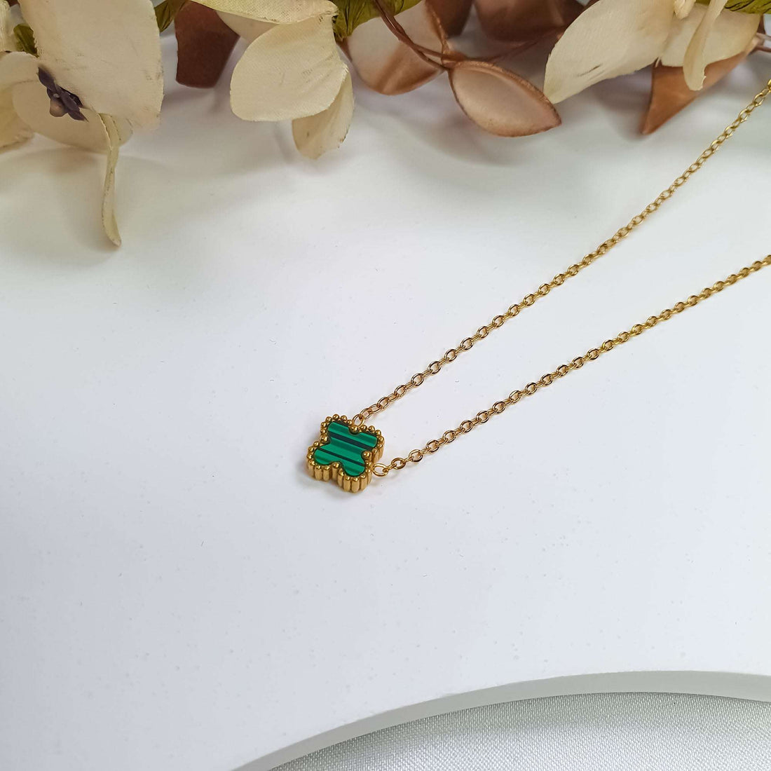 Green clover pendant close up with a gilded beaded rim beside fabric flowers