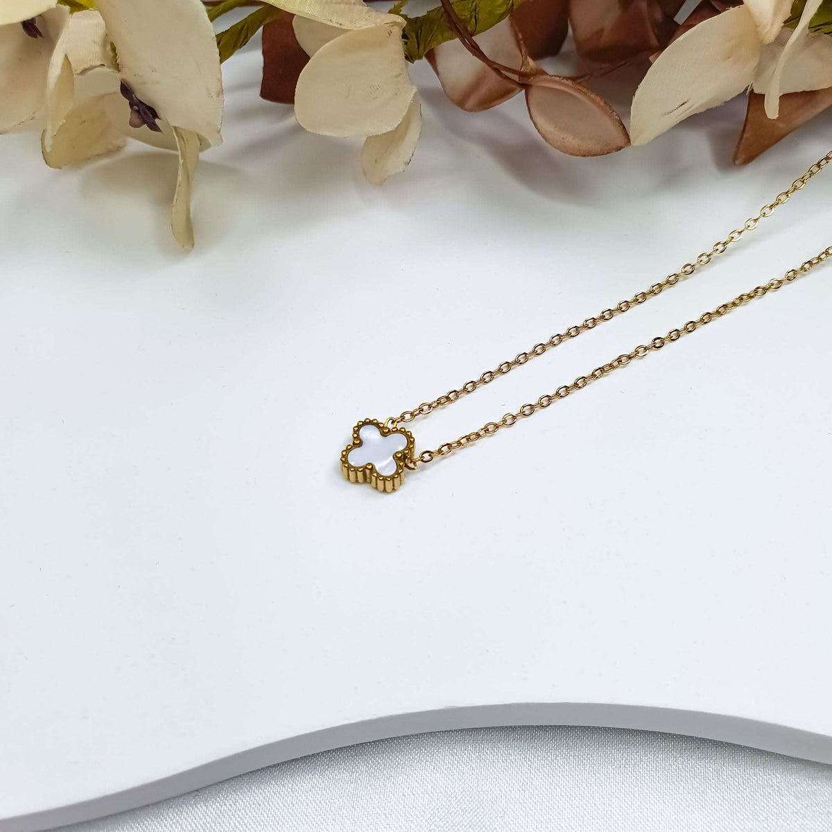 White clover pendant close up with a gilded beaded edge on a light surface