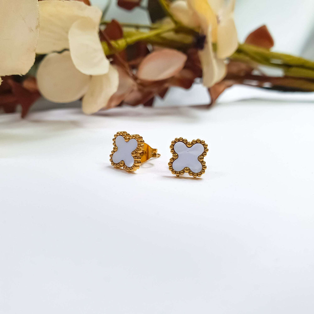 Pair of white clover earrings from the side, gold-tone post and back visible