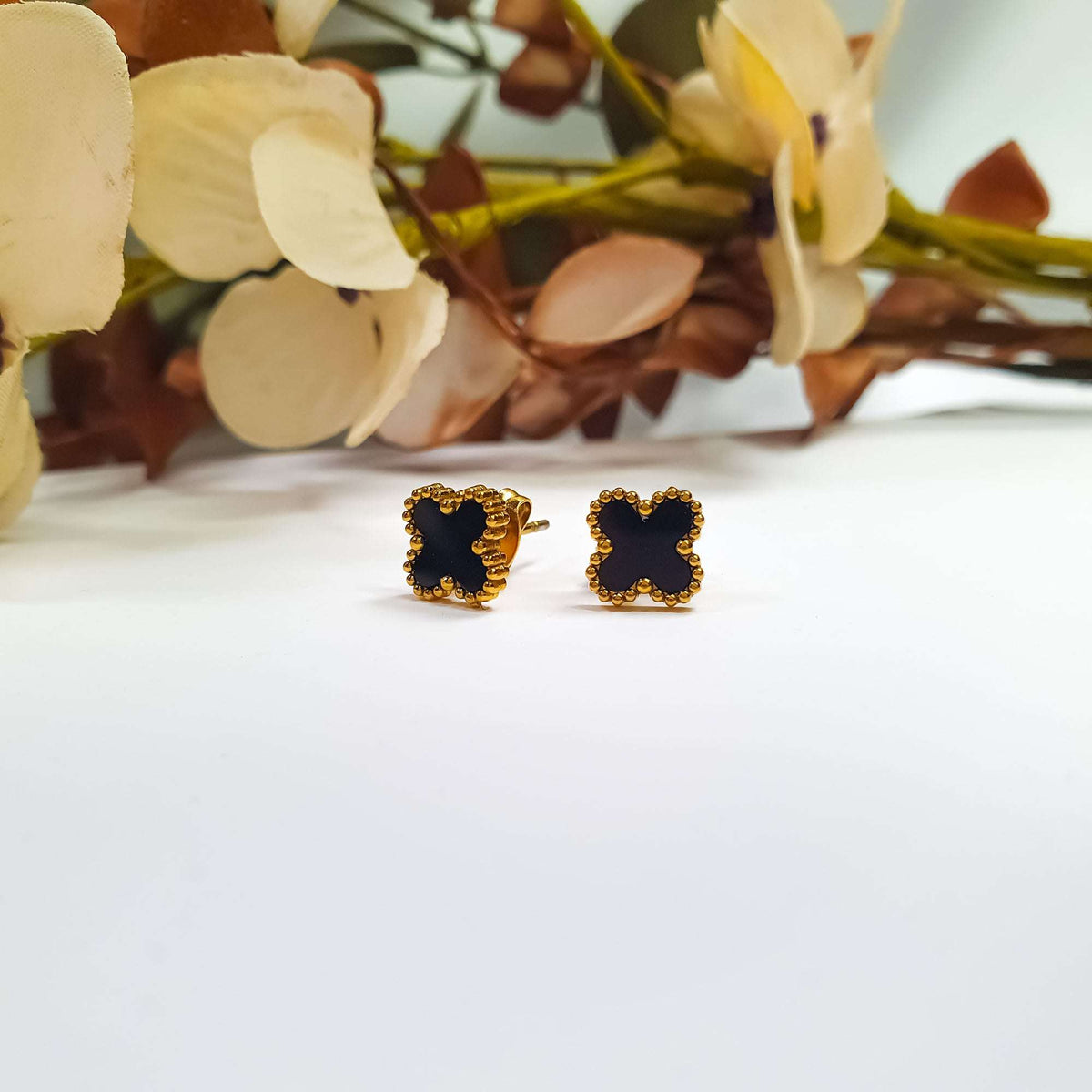 Pair of black enamel studs with gold-tone beading beside dried flowers