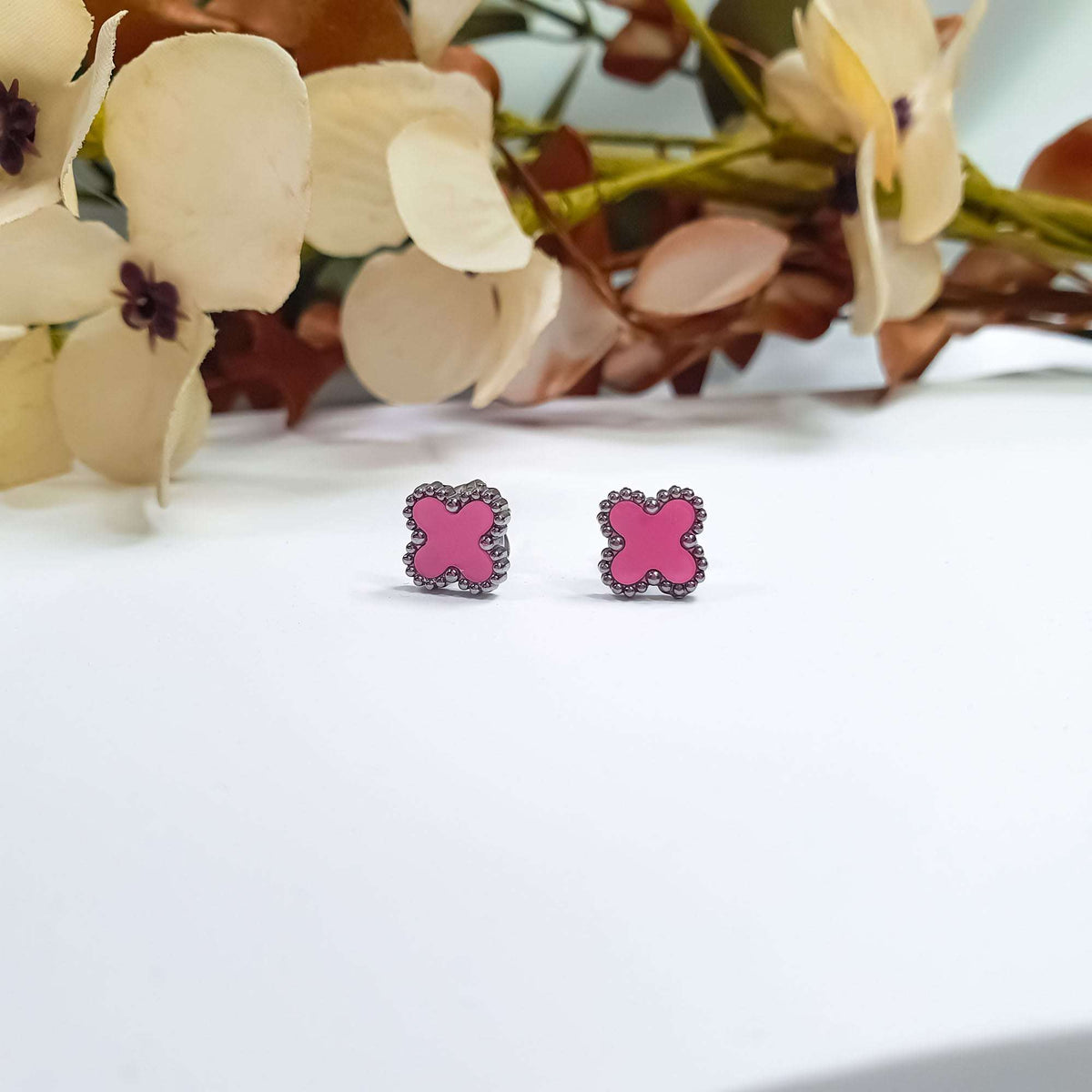Pair of pink enamel clover studs on a light background with flowers