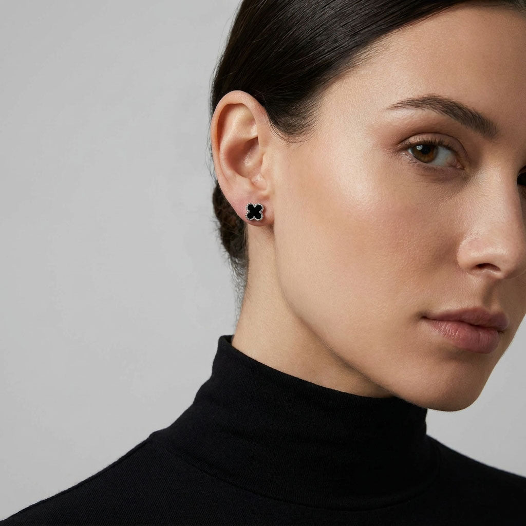 Small black clover stud with a silver-tone rim, worn with a black polo neck