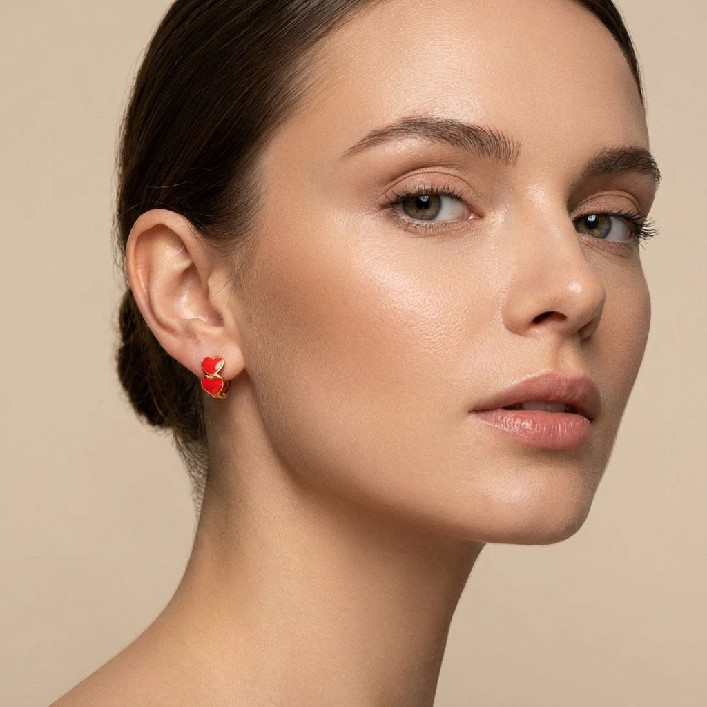 Model wearing a small gold-plated hoop with two red enamel hearts