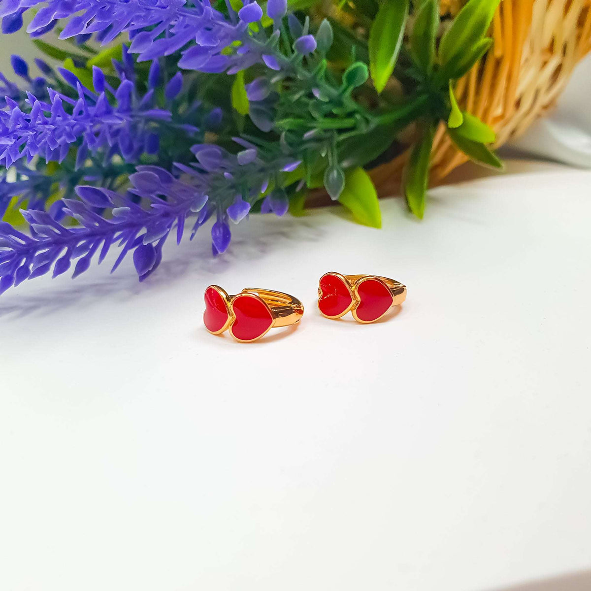 Small gold-tone hoop earrings with two red enamel hearts beside lavender
