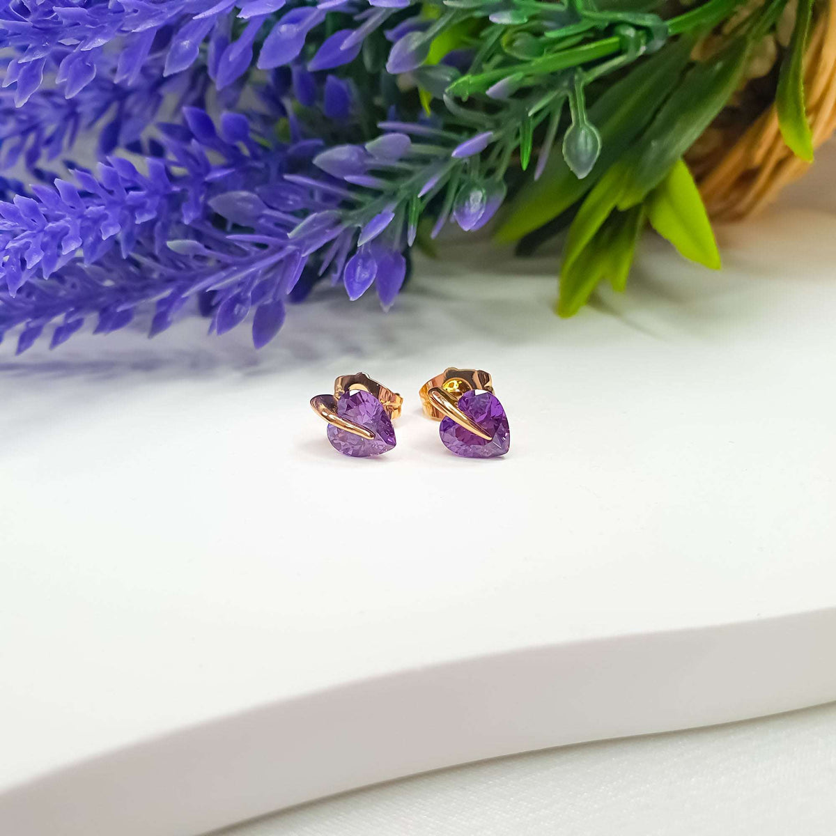Close-up of gold-tone studs with violet heart stones beside lavender