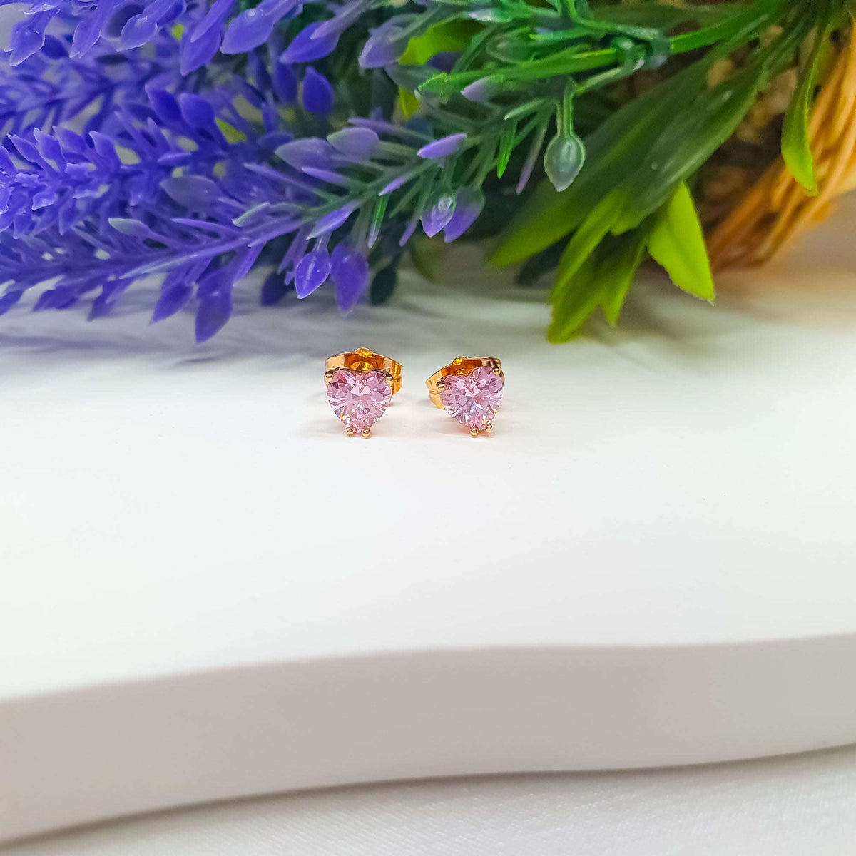 Gold-tone pink heart studs on white beside lavender flowers