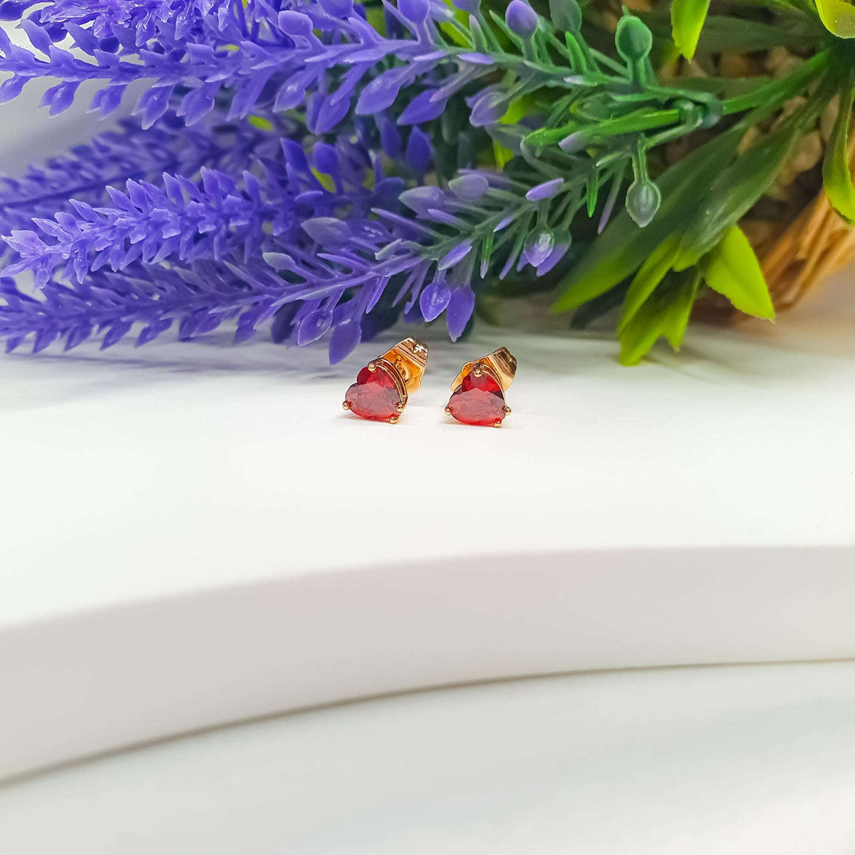 Red heart cubic zirconia studs in gold-plated settings beside lavender sprigs