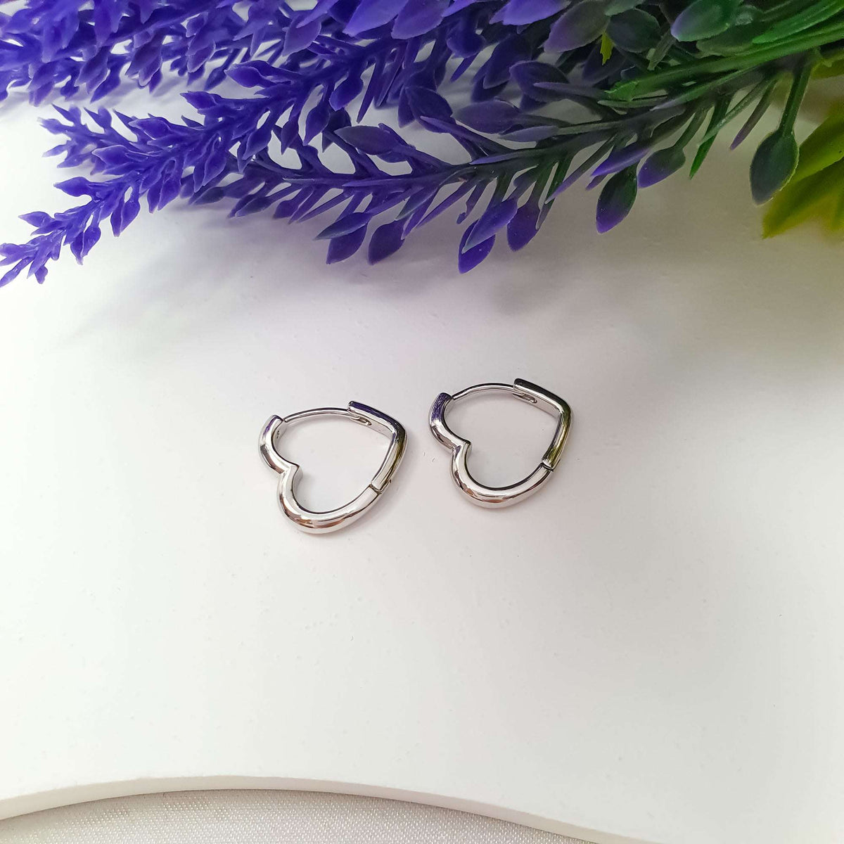 Pair of smooth silver-tone heart hoops on white beside lavender
