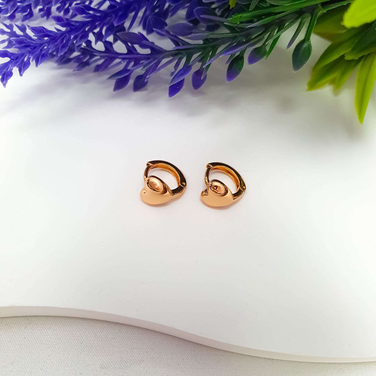 Pair of gold-tone heart hoops on white beside lavender sprigs