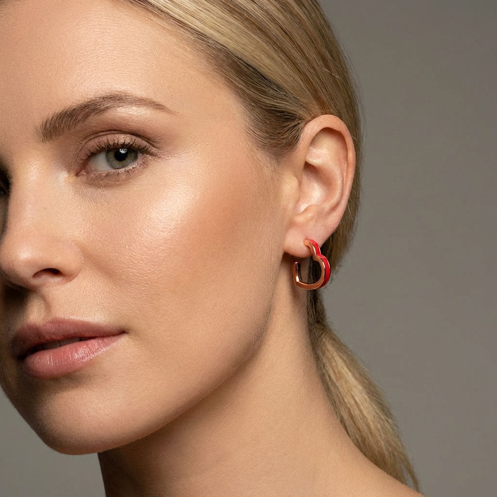 Close-up of a gold-plated heart earring with red enamel on a model
