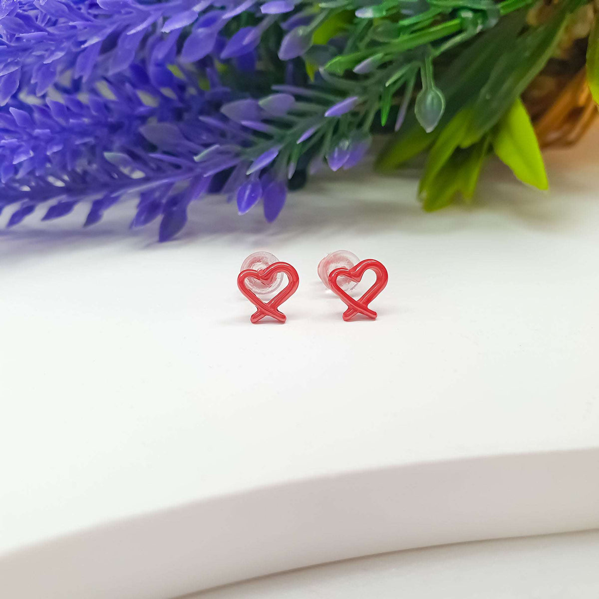 Red enamel heart studs with clear backs on white beside lavender