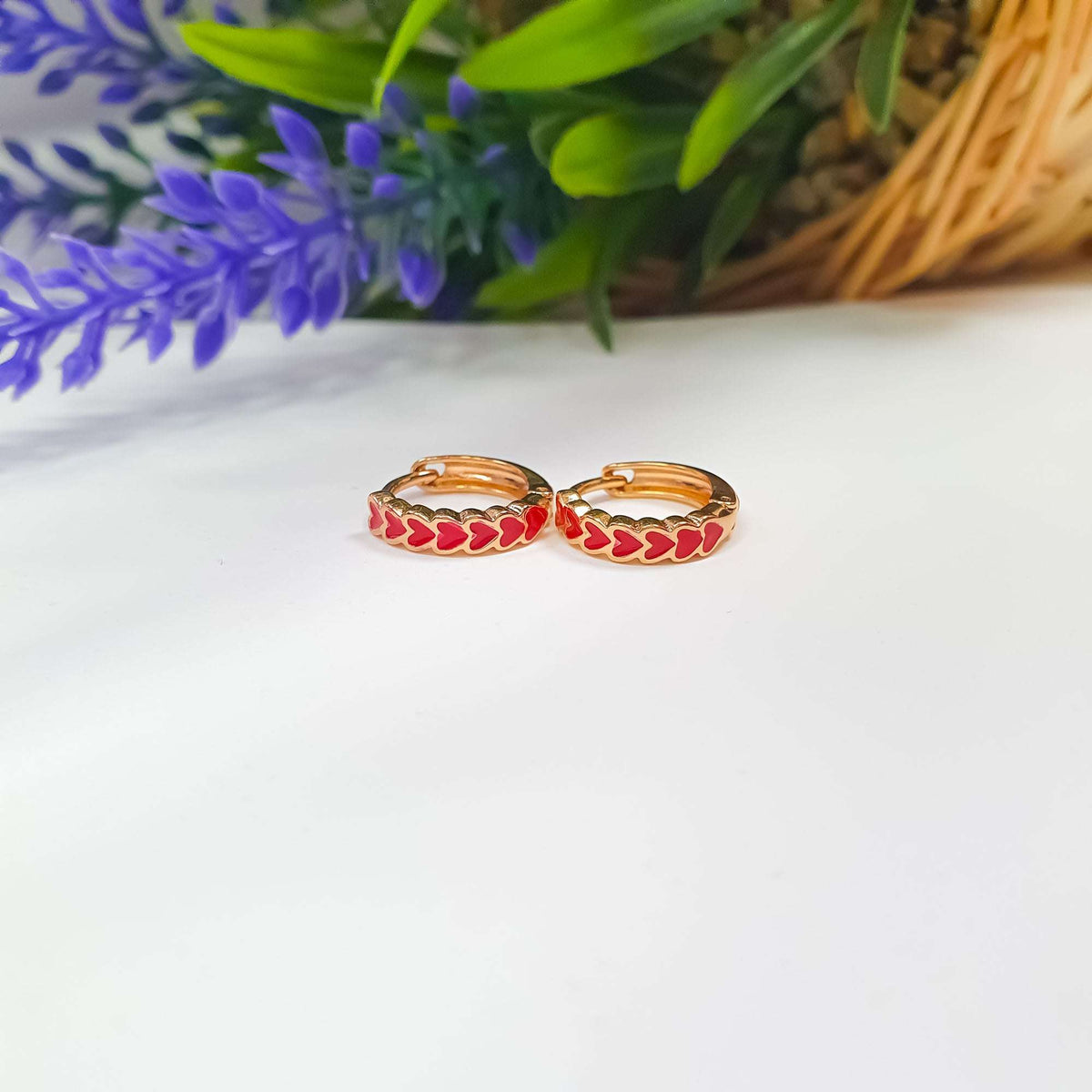 Two gold-tone hoops with red hearts lying side by side on white
