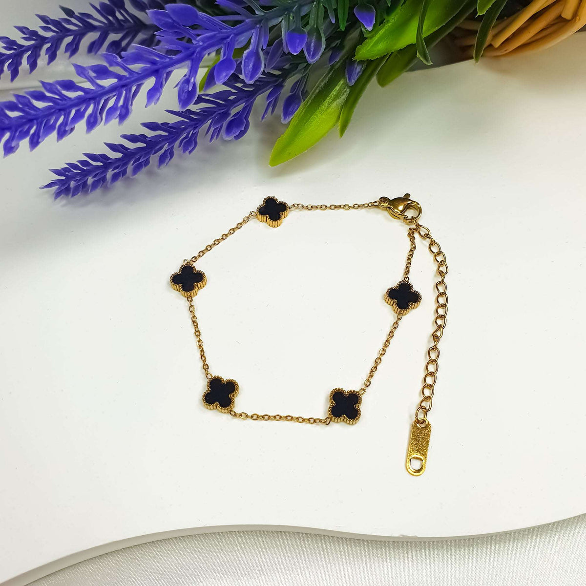 Black clover bracelet on white beside lavender with its lobster clasp visible
