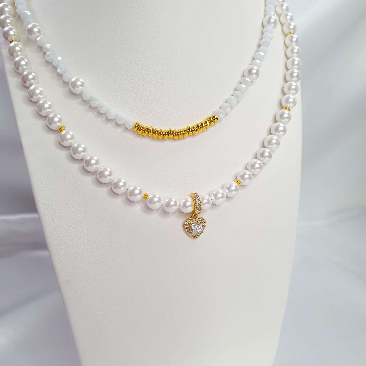White two-strand pearl necklace with a gold-tone heart on a jewellery stand