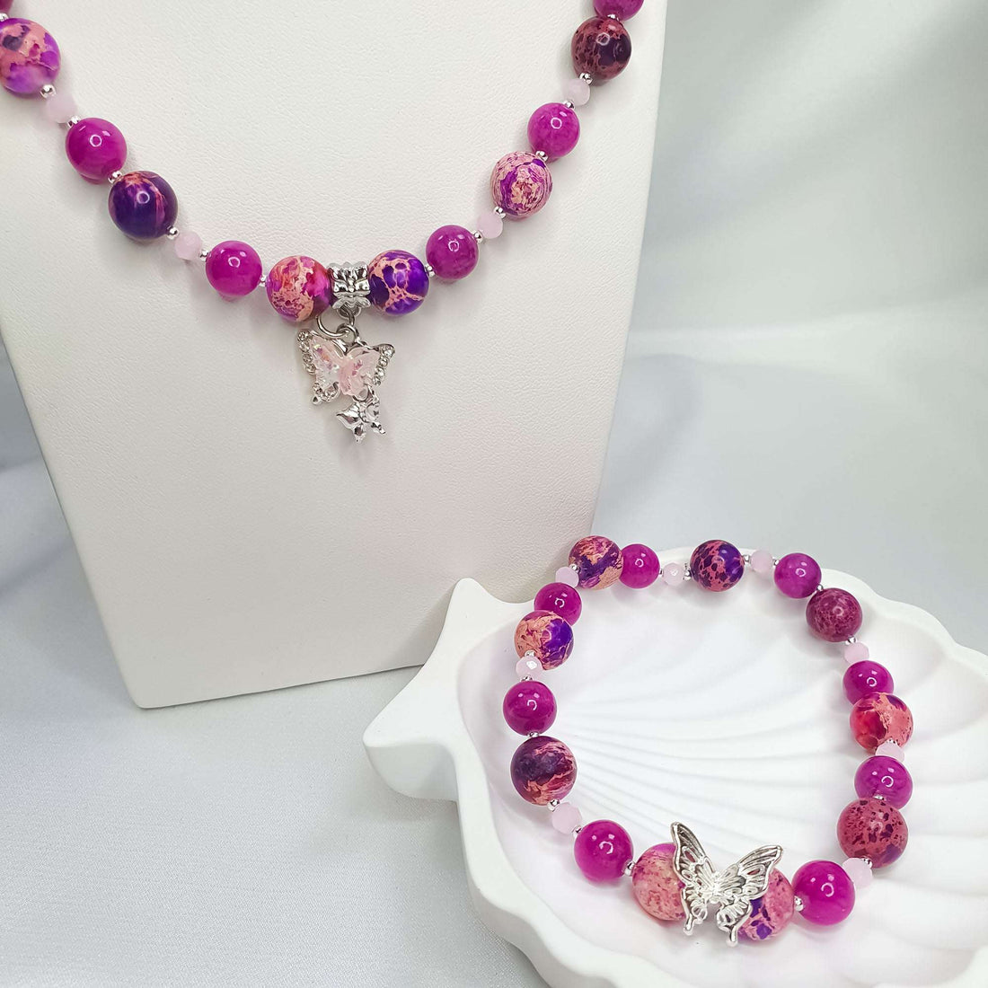 Pink bead necklace with butterfly pendant on a stand, bracelet on a shell