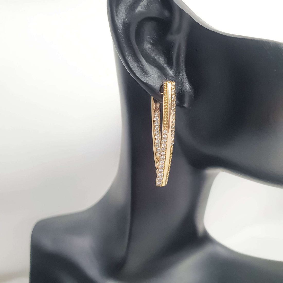 Gold-tone cubic zirconia earring on a black display ear showing its length