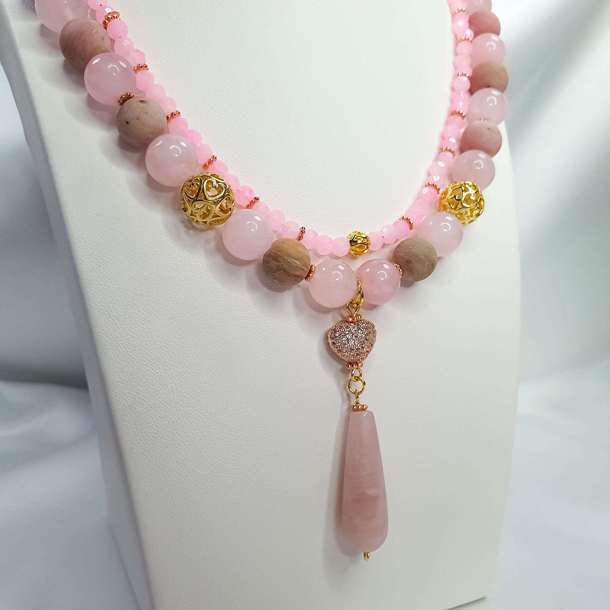 Close-up of the rose quartz necklace with patterned gold-tone beads and a teardrop pendant