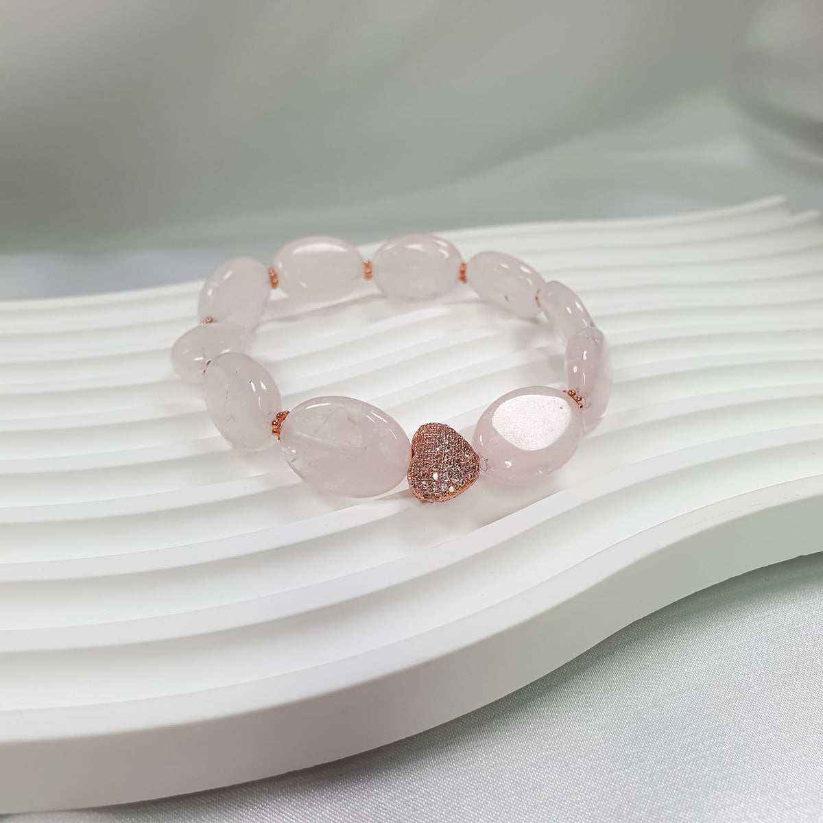 Rose quartz bracelet on a wavy white stand with a cubic zirconia heart