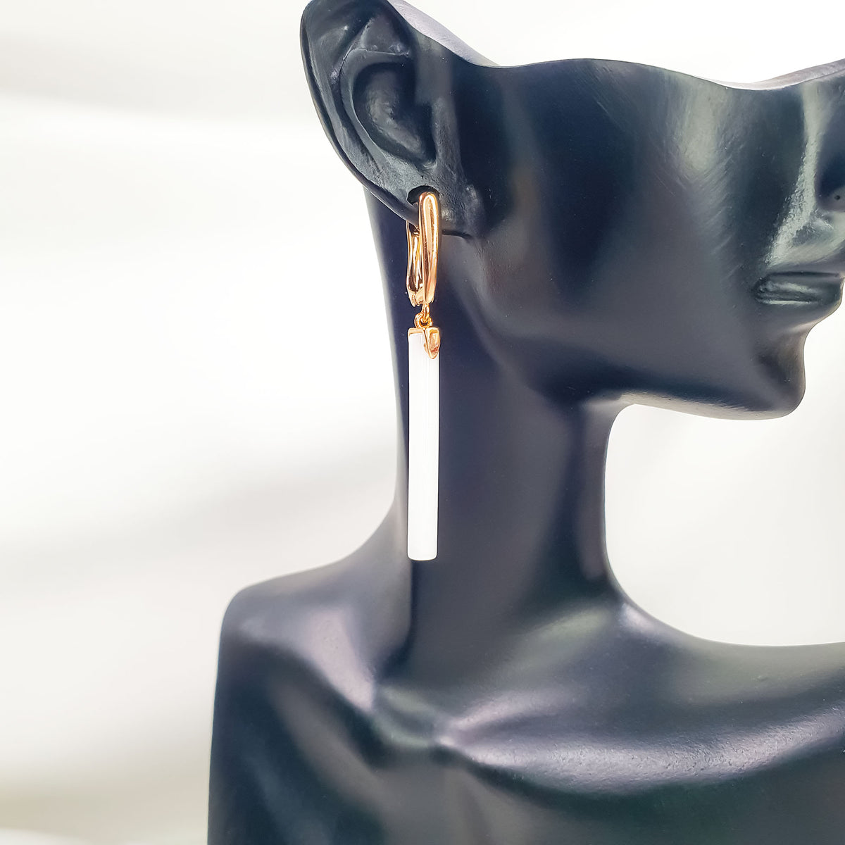Single white ceramic drop earring on a black display ear, gold-tone clasp visible