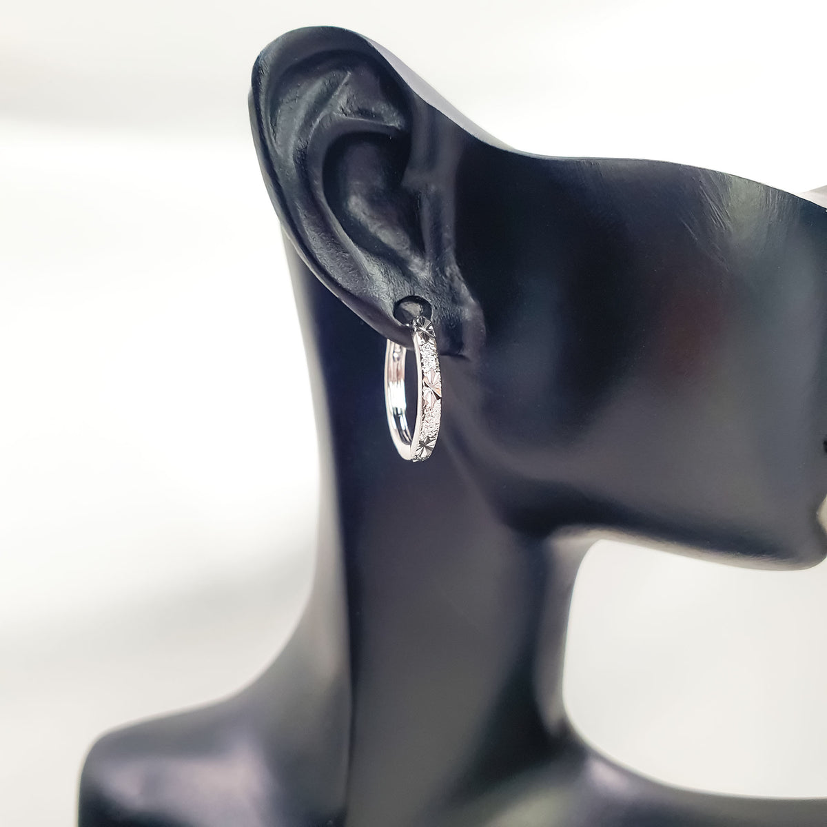 Hoop earring with a star pattern and matte texture on a black ear display