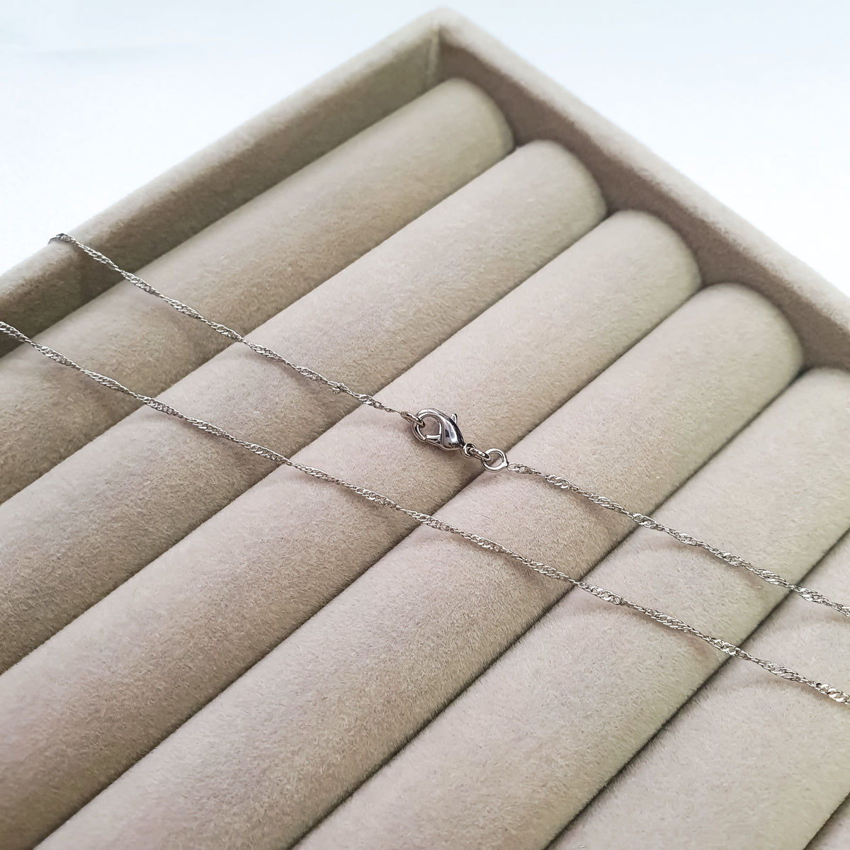 Twisted platinum-plated chain laid out on a beige velvet jewellery tray