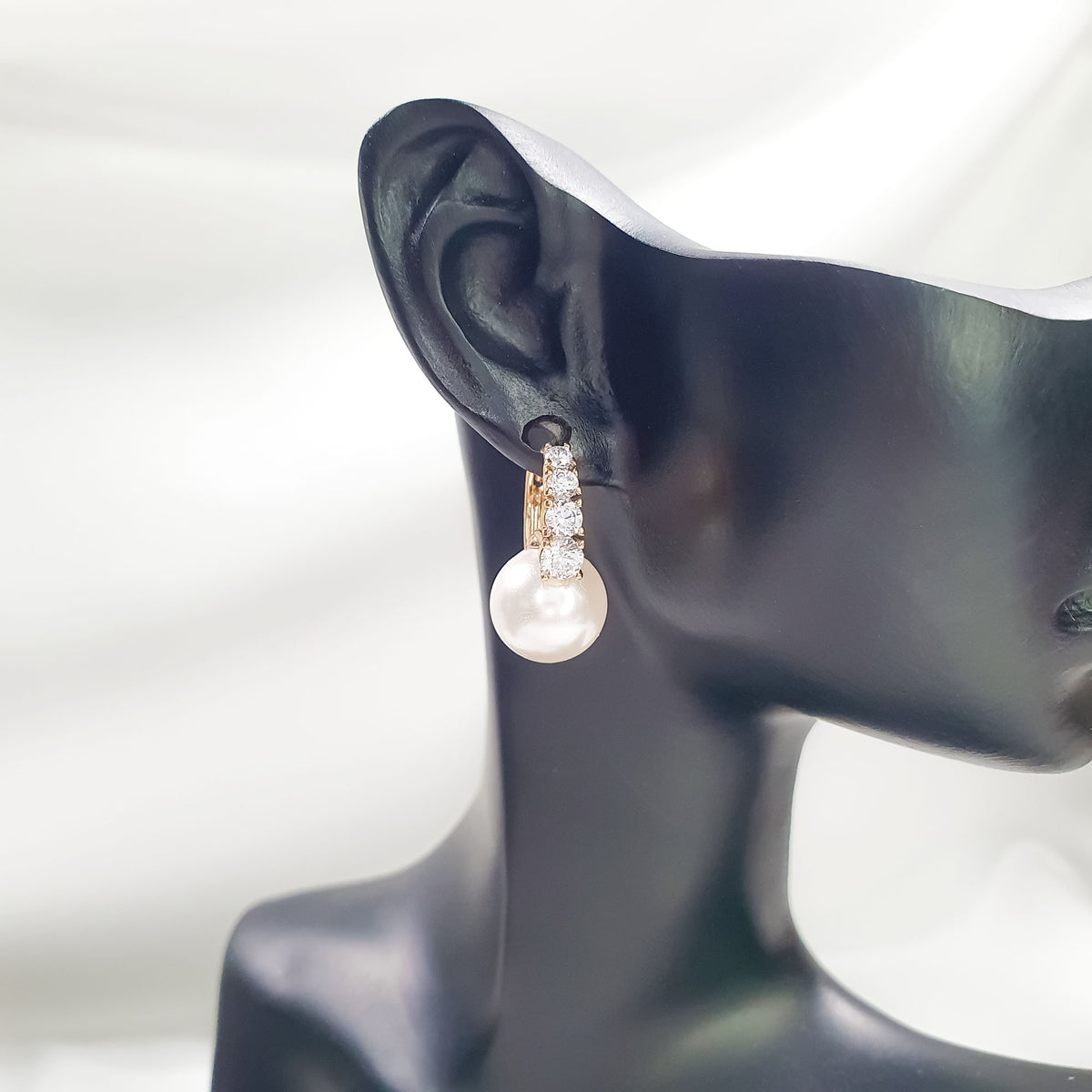 Side view of a gold-tone pearl earring on a black display ear
