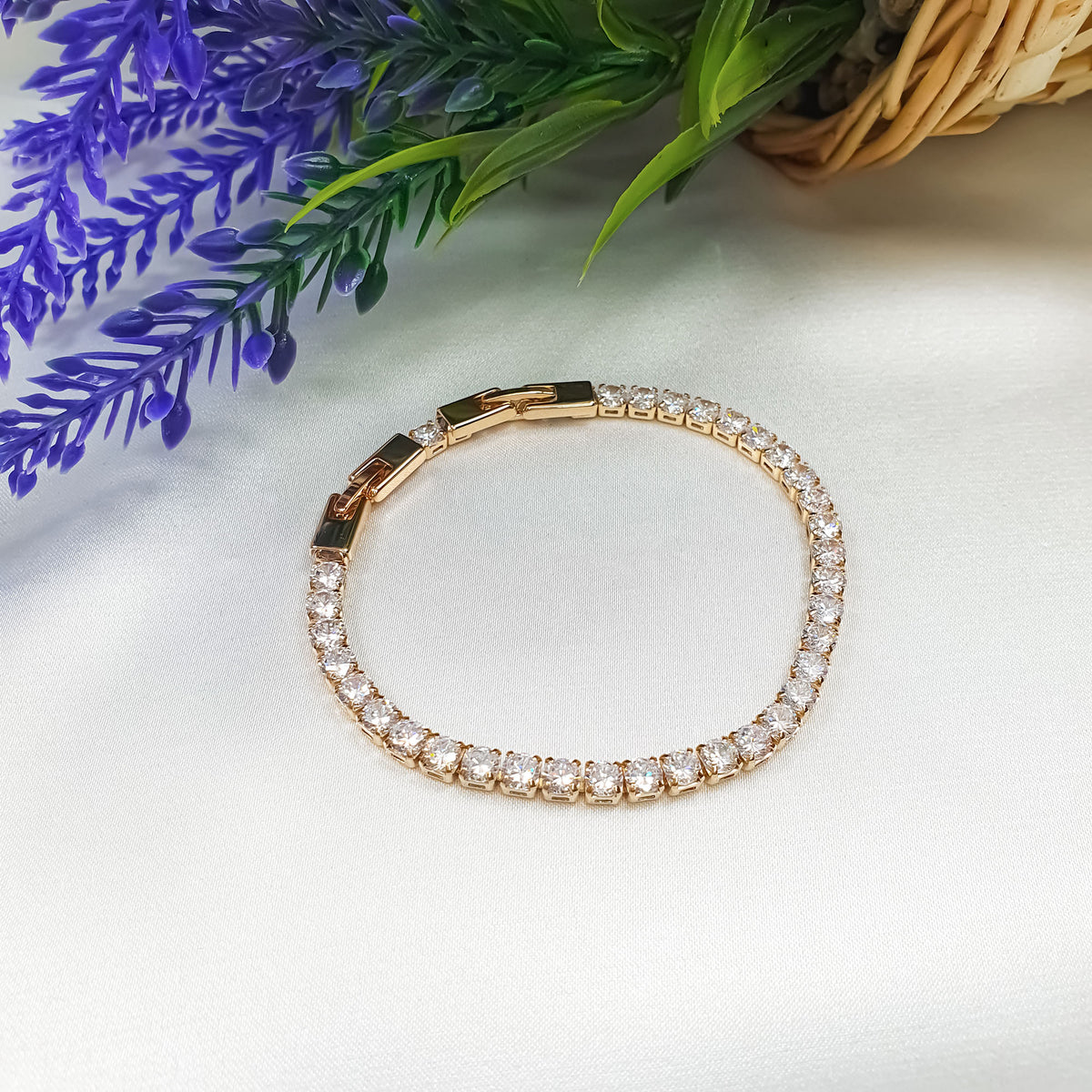 Gold-tone cubic zirconia bracelet on light fabric beside violet flowers and a basket