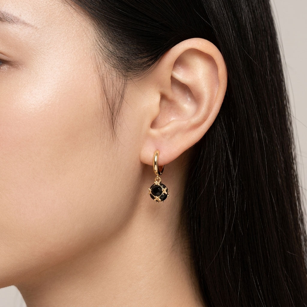 Model wearing a gold-plated hoop earring with a black cubic zirconia drop