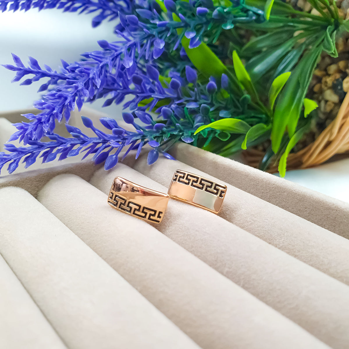 Rectangular earrings with black meander pattern and rose gold-tone finish on a velvet tray