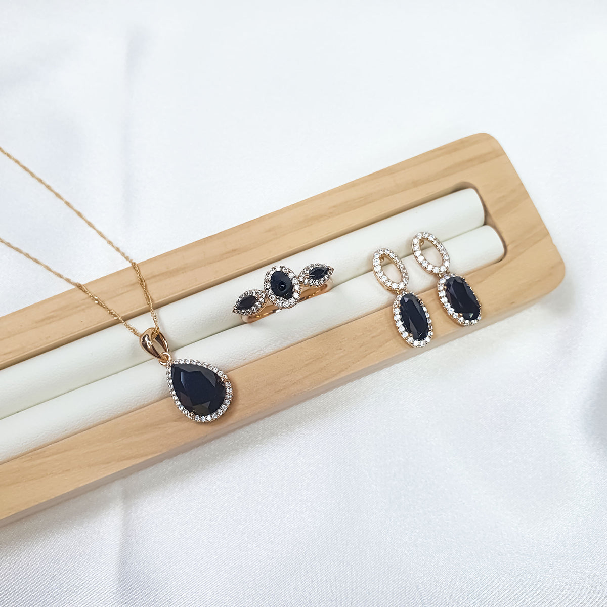 Black cubic zirconia set on a wooden stand: teardrop pendant, oval earrings, ring