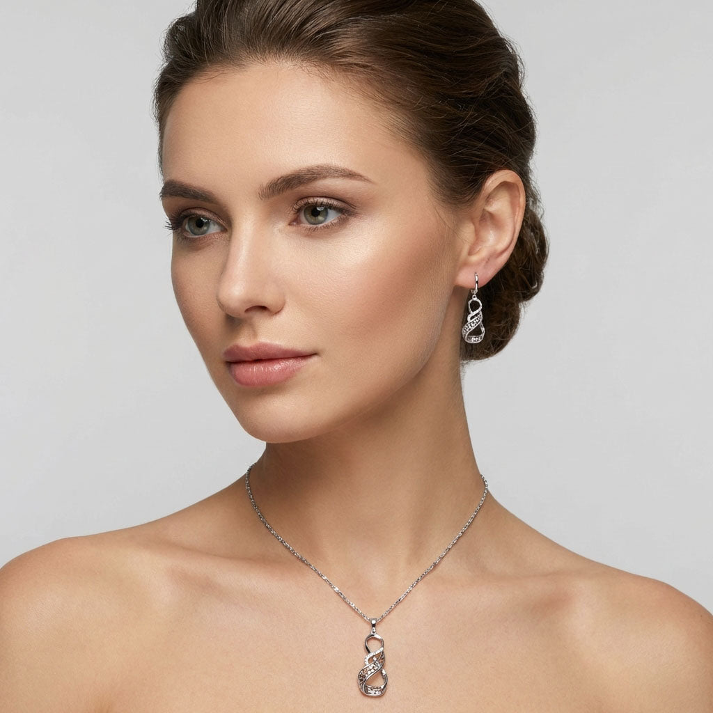 Model wearing an infinity pendant and matching earrings in silver tone, grey background