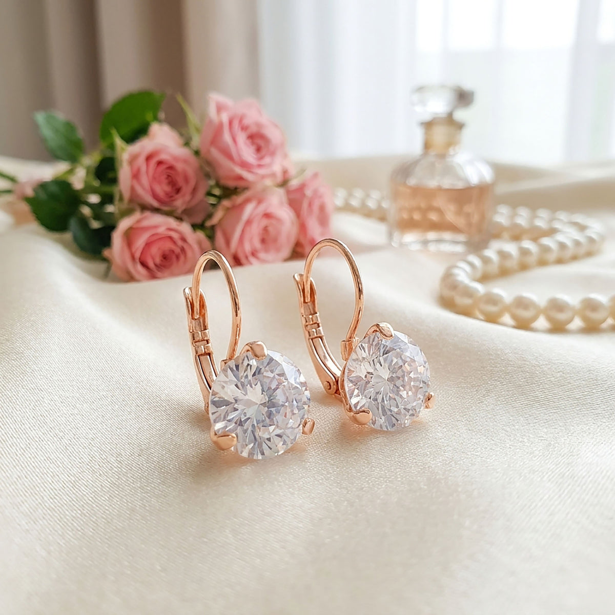 Round cubic zirconia earrings on cream satin among pink roses and pearls