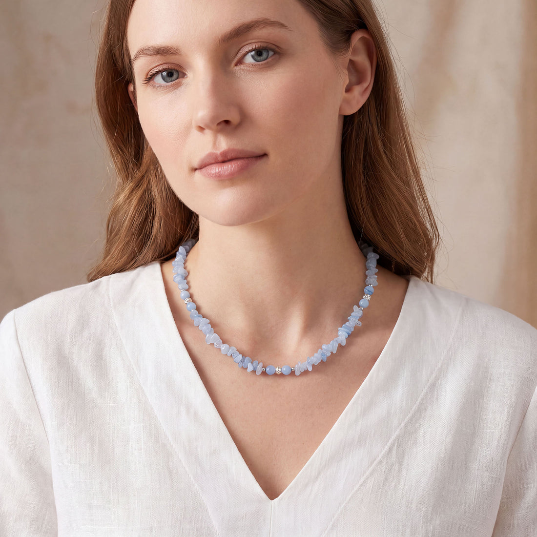 Woman in a white linen blouse wearing a light blue stone necklace