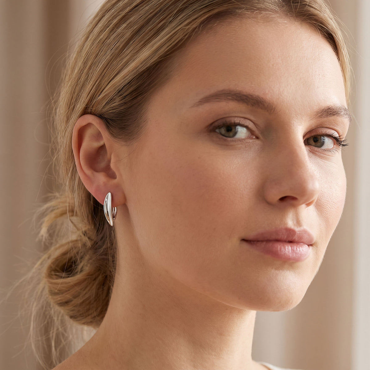 Silver | Close-up of a woman wearing smooth curved silver-tone earrings