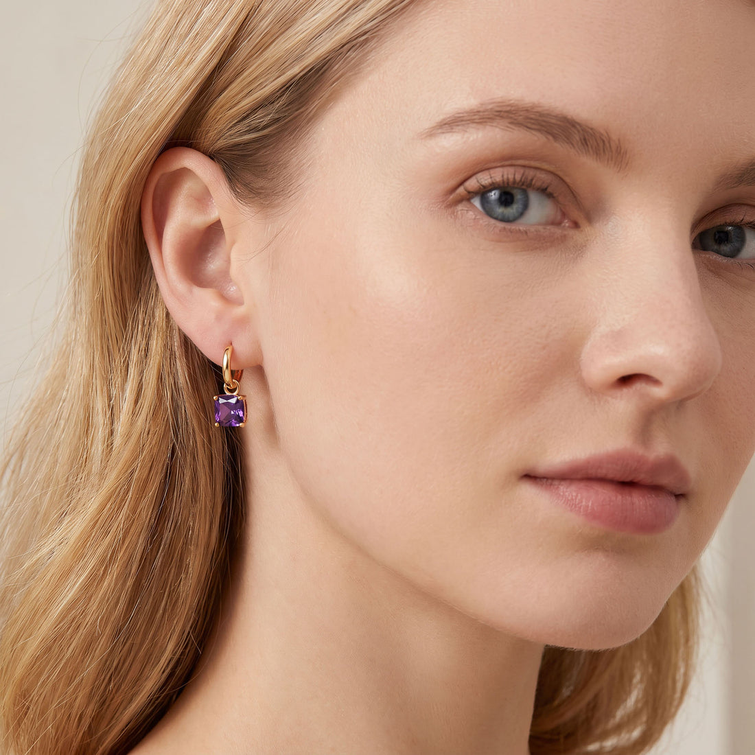 Gold | Blonde model wearing a gold-tone hoop earring with a violet crystal drop