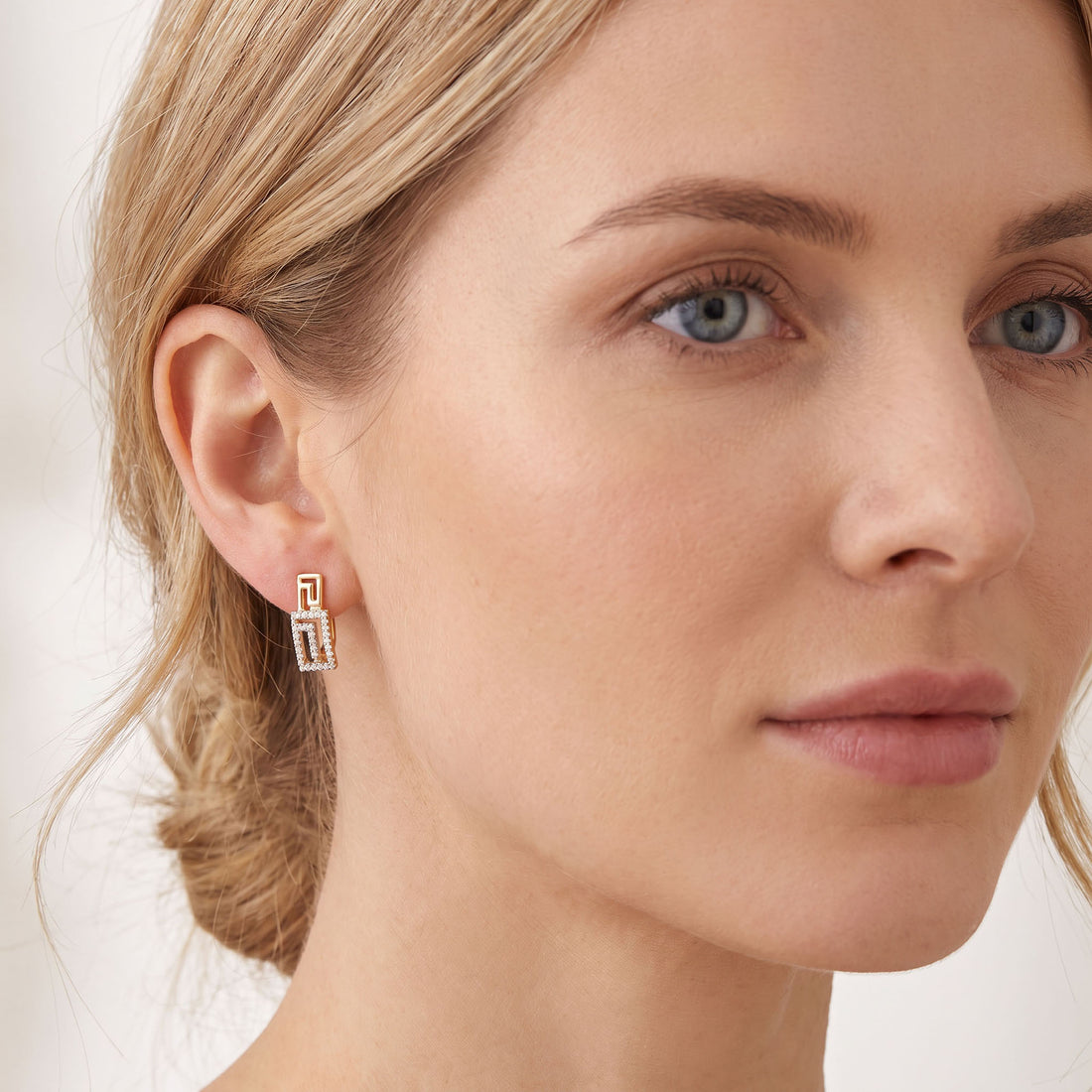 Gold-tone Greek key earring on the ear, frame below the lobe