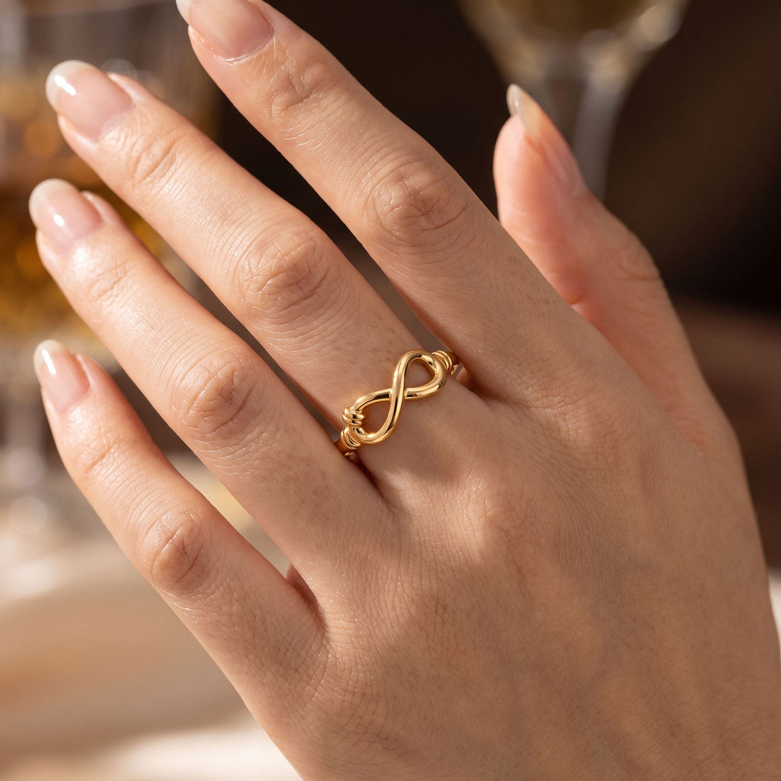 Gold-tone infinity symbol ring worn on a woman's finger