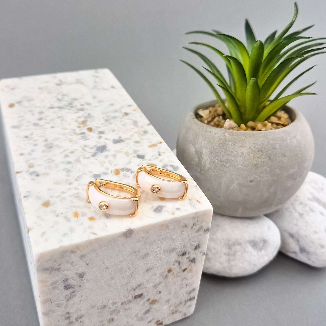 White ceramic and gold-plated earrings in side view on a light stone block