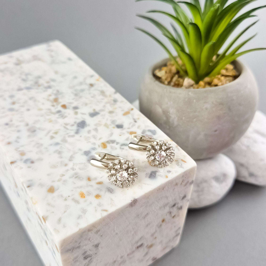 Flower earrings with leverback clasps on a light stone beside a small succulent