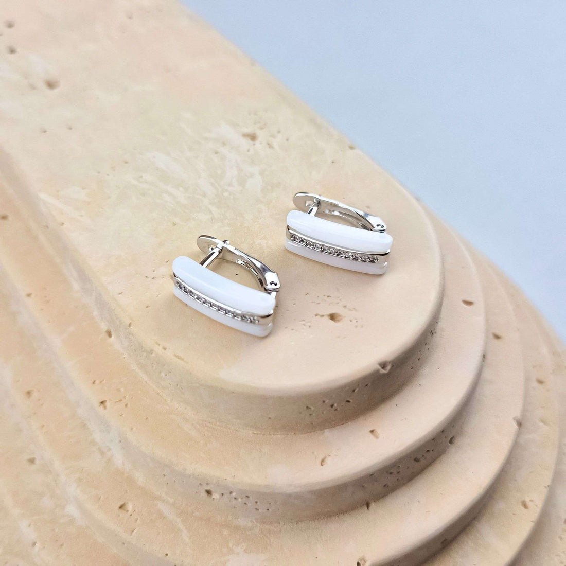White ceramic earrings with cubic zirconia on a sand-coloured stone stand, leverback visible