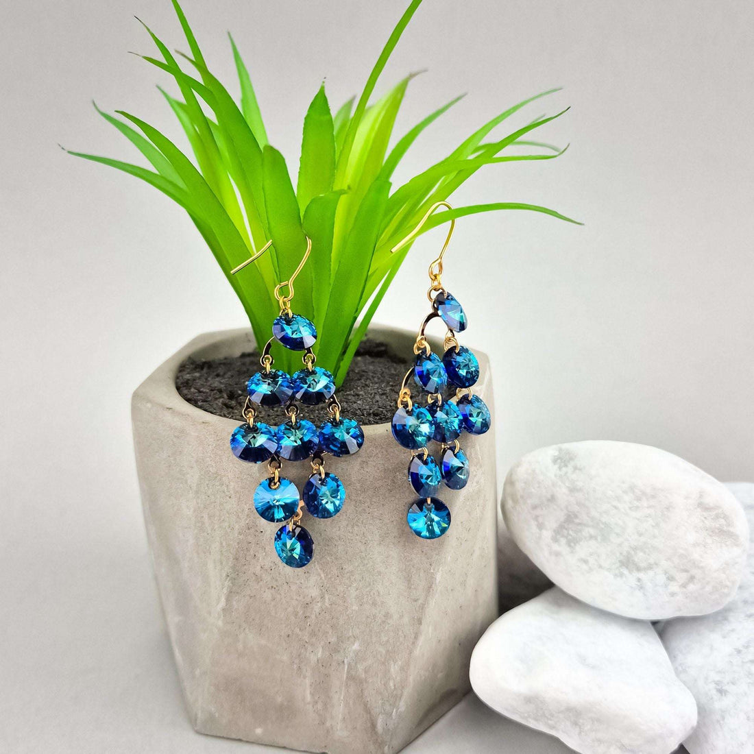 Blue cascade earrings beside a concrete plant pot, gold-plated hooks visible
