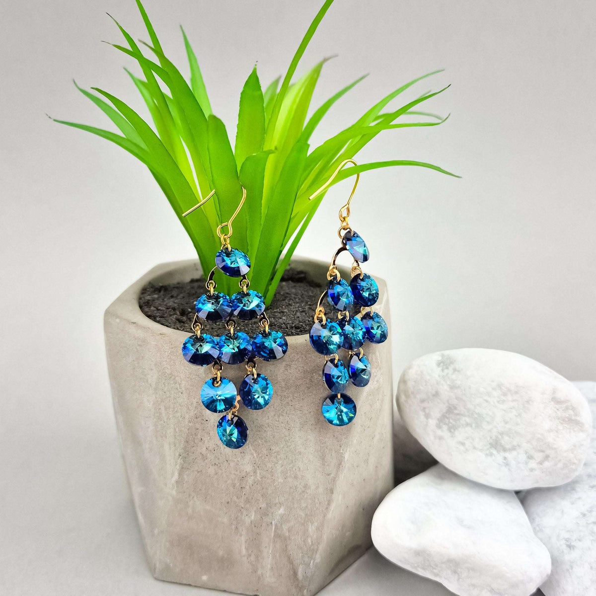 Blue cascade earrings beside a concrete plant pot, gold-plated hooks visible
