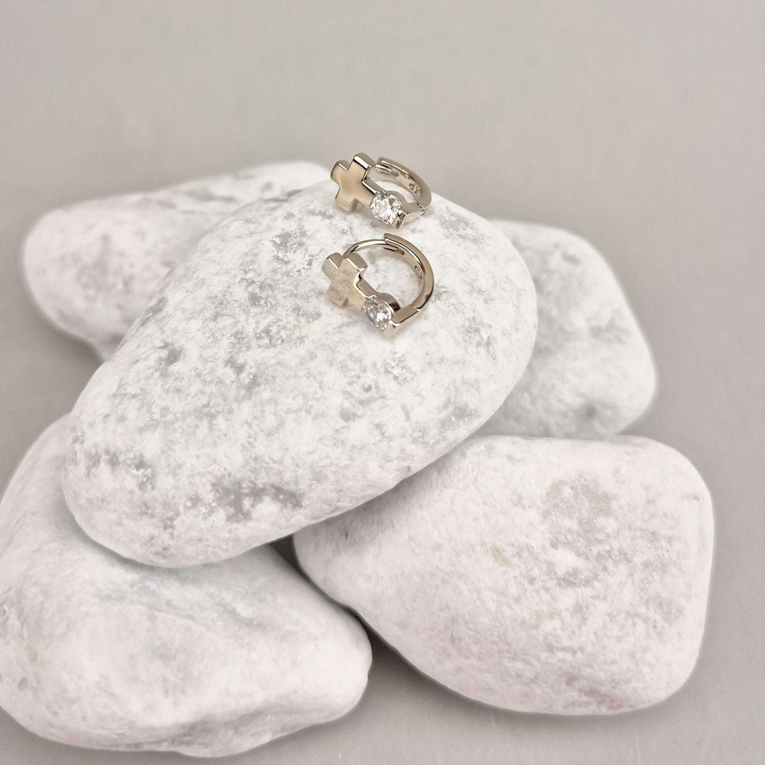 Silver-tone cross earrings with leverback clasps, side view on white pebbles