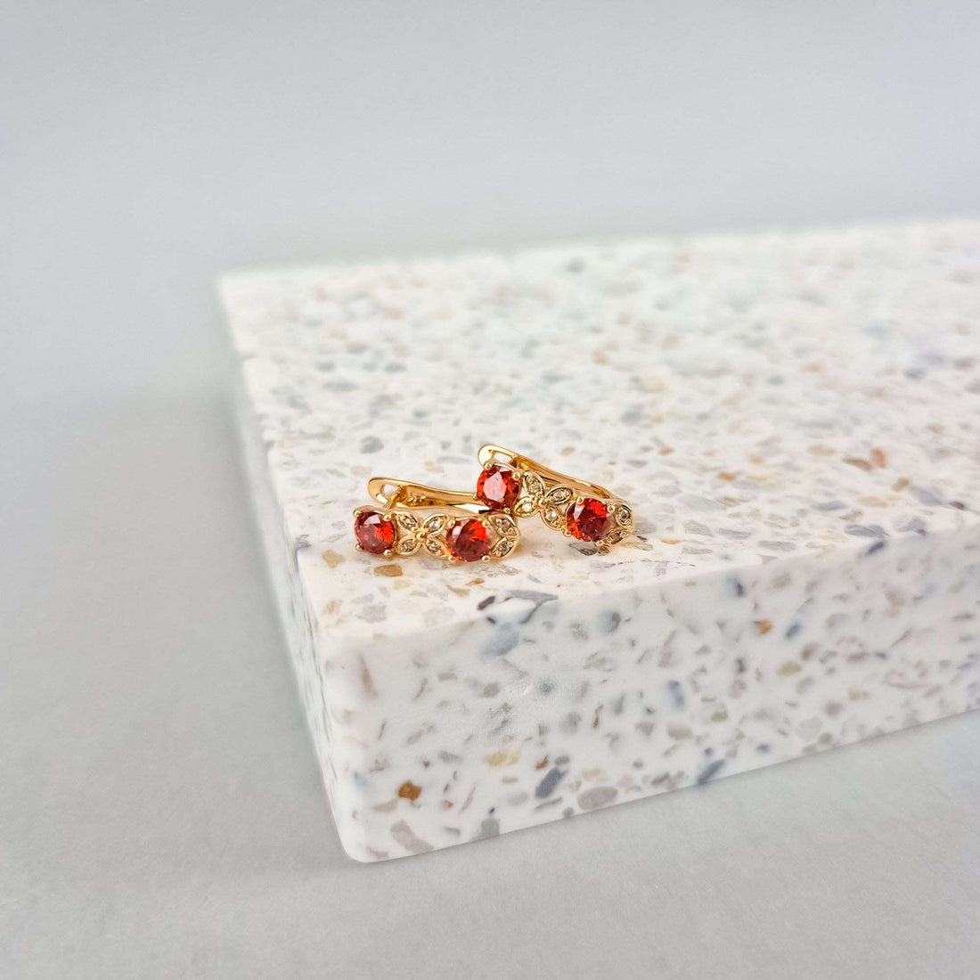 Red crystal earrings in gold tone on a white speckled stone stand, clasp visible