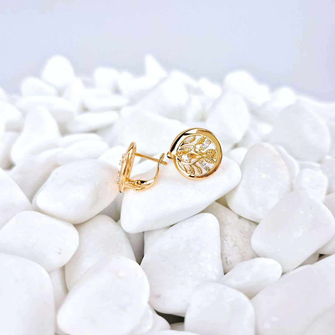 Gold-plated earrings in side view on white pebbles, leverback clasp and zirconia visible